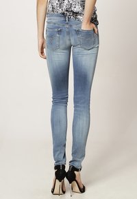 Jeans ajustados de color azul claro con un acabado desgastado, que cuentan con dos bolsillos traseros y una cremallera, combinados con zapatos de tacón negros.