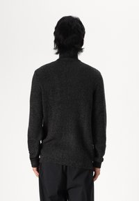 Dark grey knitted sweater with a high collar and ribbed texture. Long sleeves and a relaxed fit, featuring a seamless design at the back.