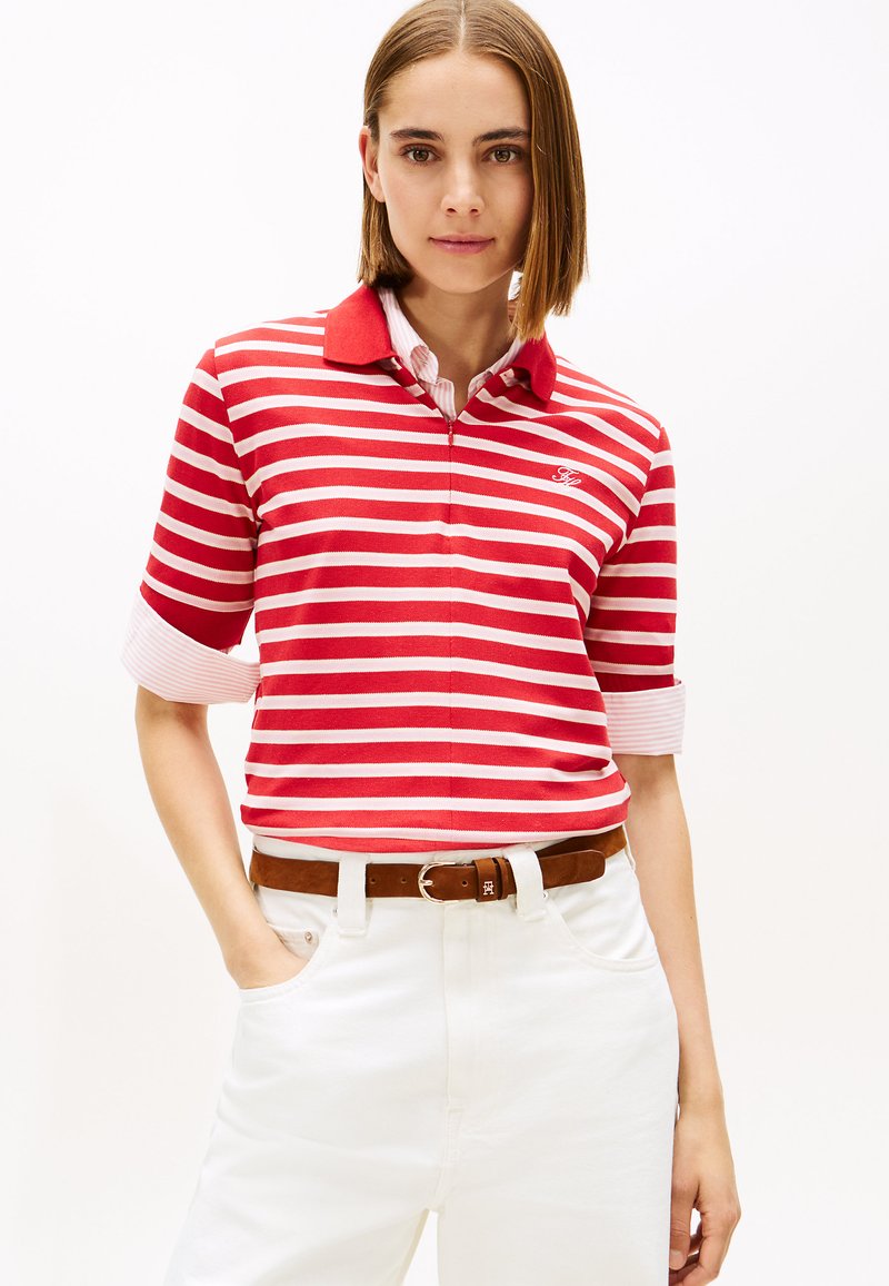 Punaste ja valgete triipudega polost särgi, millel on punane ühtlane krae ning rullitud varrukad, kombineeritud valgete pükste ja pruuni vööga.