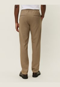 Pantalones marrones de textura con un ajuste relajado, que presentan una goma en la cintura y dos bolsillos traseros. Llevados con calzado negro.
