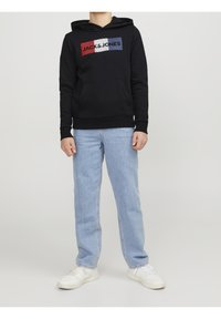 Felpa nera con un logo multicolore e tasca a marsupio, abbinata a jeans a gamba dritta azzurri e sneakers bianche.