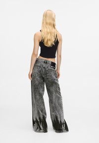 Wide-leg jeans in black and gray wash with a dripped pattern at the hem. Features a branded patch on the waistband and a relaxed fit.