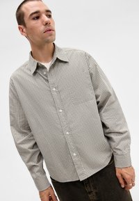 Loose-fitting button-up shirt in gray with small check pattern, featuring a pointed collar, long sleeves, and single chest pocket.