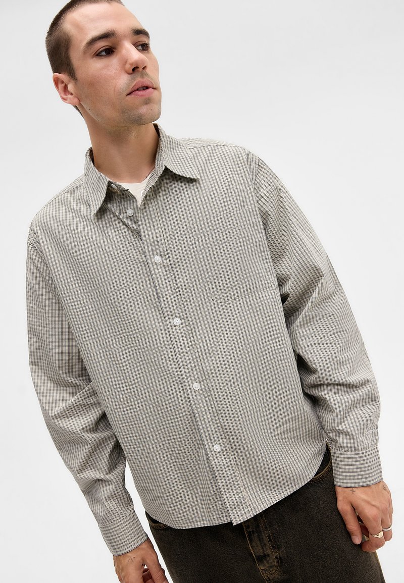 Loose-fitting button-up shirt in gray with small check pattern, featuring a pointed collar, long sleeves, and single chest pocket.