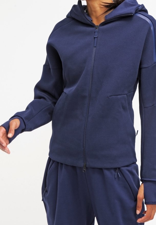 Marinblå zip-up hoodie med fodrad huva, framficka och ribbade muddar. Tillverkad av mjukt material med en slät textur och subtila designdetaljer.