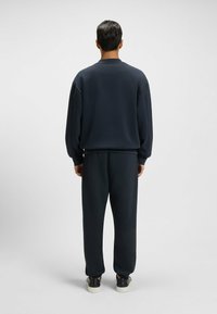 Navy blue sweatshirt and pants set, featuring a relaxed fit and ribbed cuffs. Material appears soft and textured, with simple design elements.
