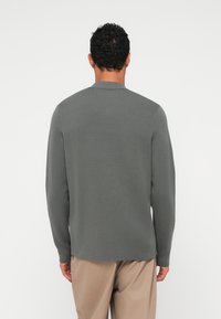 Grå langermet strikkegenser med avslappet passform, med en subtile tekstur og rundet kant, kombinert med beige bukser.