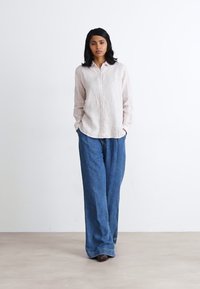 Light pink striped button-up shirt paired with loose, wide-leg dark blue denim pants. Smooth texture with a casual, relaxed fit.