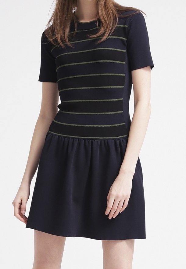 Femme portant une robe bleu marine à manches courtes avec des rayures horizontales vert olive sur le corsage supérieur et une jupe froncée.