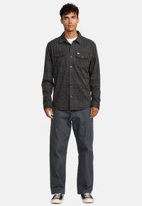 Geruite button-up shirt in donkergrijs met blauwe accenten, twee borstzakken; gecombineerd met losse grijze broek en zwarte sneakers.