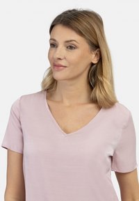 Jasnoróżowa krótko-sleeve bluzka z dekoltem w kształcie litery V, wykonana z gładkiego materiału. Posiada luźny fason z minimalnymi detalami szewnymi.