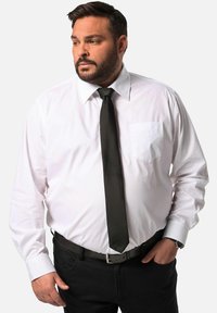Camicia bianca a maniche lunghe con taschino sul petto, abbinata a una cravatta nera e pantaloni neri. Caratterizzata da un colletto classico e una texture di tessuto liscia.