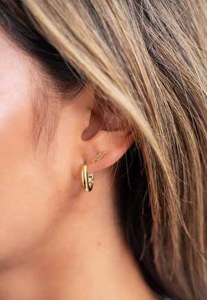 Orecchino a cerchio in oro con una finitura lucida e un sottile chiodo d'oro. L'orecchino è circolare mentre il chiodo è dritto e dal design minimalista.