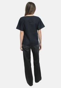 Top corto blu navy a maniche corte con scollatura quadrata, abbinato a jeans neri a vita alta a palazzo con tasche posteriori visibili.