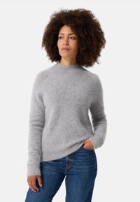 Maglione grigio chiaro e morbido con maniche lunghe e scollatura rotonda, abbinato a jeans in denim blu; texture soffice e vestibilità rilassata.