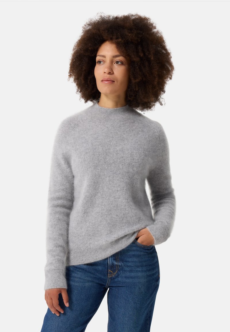Maglione grigio chiaro e morbido con maniche lunghe e scollatura rotonda, abbinato a jeans in denim blu; texture soffice e vestibilità rilassata.