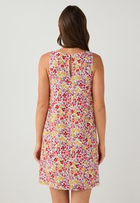 Bloemrijk jurkje met een mouwloos ontwerp, voorzien van een meerkleurig patroon van rode, gele en groene bloemen op een witte achtergrond. Details met een sleutelgat aan de achterkant.