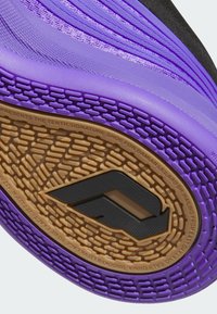 Fialová sportovní bota s vyraženým vzorem na podrážce, s texturovaným svrškem a černými akcenty. Výrazné logo v černé barvě na zlatém pozadí.