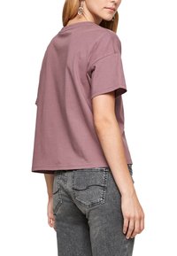 Krátkoslá t-shirt s cropped střihem ve stálem růžovém barvě z bavlny. Má kulatý výstřih a čistý lem. Je kombinována s těsnými šedými džíny.