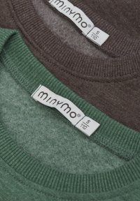 Två tröjor staplade, en mörkbrun och en mörkgrön. Båda har ribbade kragar och tygmärken som är synliga med varumärke och storleksdetaljer.