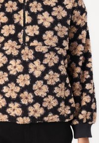 Sudadera de forro polar con diseño de media cremallera, que presenta un fondo negro y un patrón floral marrón claro; puños y dobladillo acanalados.