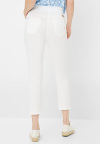 Witte cropped broeken met een gladde textuur, voorzien van twee achterzakken en metalen knoopaccenten, gecombineerd met lichte espadrilles.