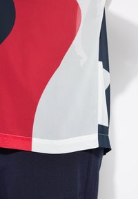Top colorato a maniche corte con forme astratte rosse, bianche e blu navy, realizzato in un tessuto leggero con una texture morbida.