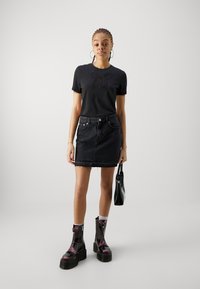 Black short-sleeve t-shirt with embroidered butterfly design, paired with a high-waisted black denim skirt and chunky black ankle boots.