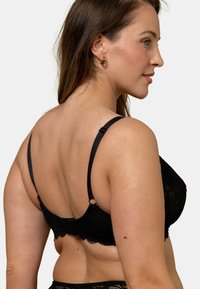 Soutien-gorge en dentelle noire avec des bretelles réglables, une fermeture à crochets et œillets, et des bordures en dentelle festonnées, mettant en valeur un motif floral et une texture douce.