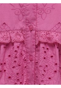 Roze geborduurd kledingstuk met een knoopsluiting aan de voorkant, kantafwerking en decoratieve uitsnijdingen met ingewikkelde details.
