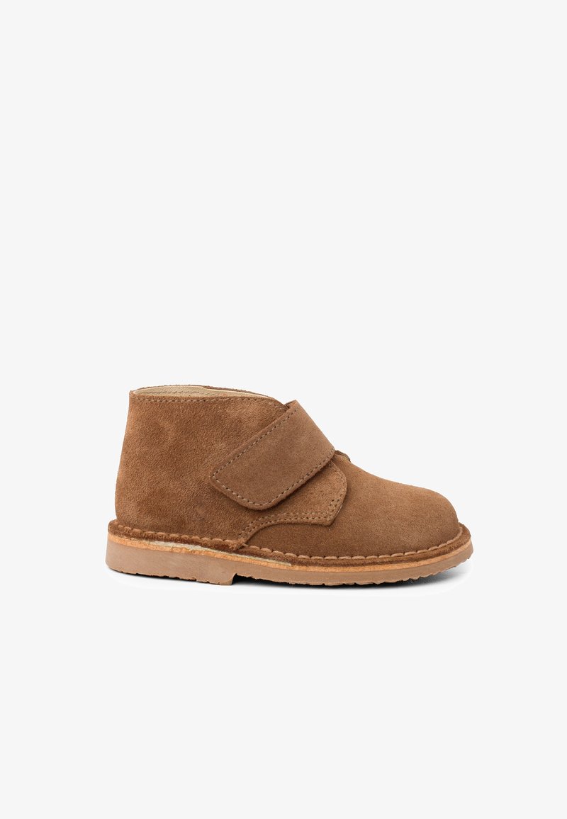 Chaussure bébé en suède marron avec une large bande velcro et une semelle en caoutchouc cousue, montrée de profil sur fond blanc.