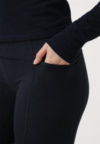 Čierne športové legíny s vreckom, vyrobené z elastického materiálu. Majú ploché švy a hladkú textúru, navrhnuté pre pohodlie a pohyblivosť.