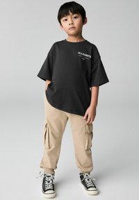 Svart kortärmad t-shirt med texten "ALLSAINTS". Tillsammans med beige cargo-byxor som har sidofickor och elastiska muddar, samt svarta sneakers.