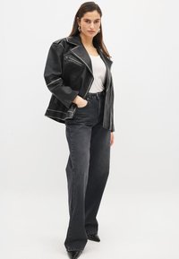 Veste de biker en cuir noir avec des coutures blanches contrastantes, associée à un jean en denim sombre taille haute et des escarpins noirs à bout pointu.