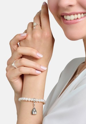 Silberarmband mit Perlen und einem detaillierten Charme. Das Modell trägt einen dünnen Silberring in Sternform und einen Ring mit Perlenakzent. Heller rosa Nagellack.