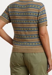 Stickad kortärmad tröja i beige med texturerade ränder i blått, grönt och gult. Ribbad krage och nederkant. Bärs tillsammans med olivgröna byxor.