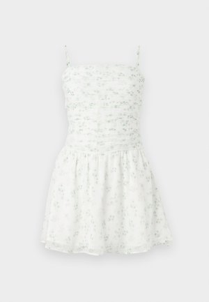 Vit blommig klänning med gröna accenter, som har en smockad byst, tunna axelremmar och en utsvängd kjol. Lätt, luftig tyg med ett delikat mönster.