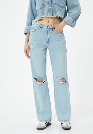 Jean en denim bleu clair avec une coupe ample, présentant de grandes déchirures usées au niveau des genoux et un ourlet effiloché. Taille mi-haute.