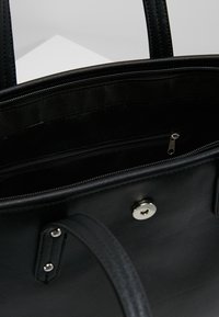 Czarna torebka z gładką fakturą, zamykaną na zamek kieszenią wewnętrzną, zapięciem na zatrzask i podwójnymi uchwytami. Minimalistyczny design bez widocznych zewnętrznych detali.