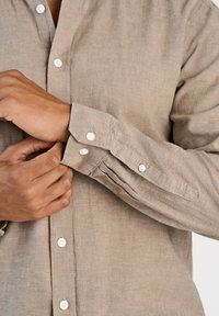 Camicia in lino beige con colletto abbottonato. Bottoni bianchi decorano i polsini e la patta frontale. Tessuto liscio, maniche lunghe.