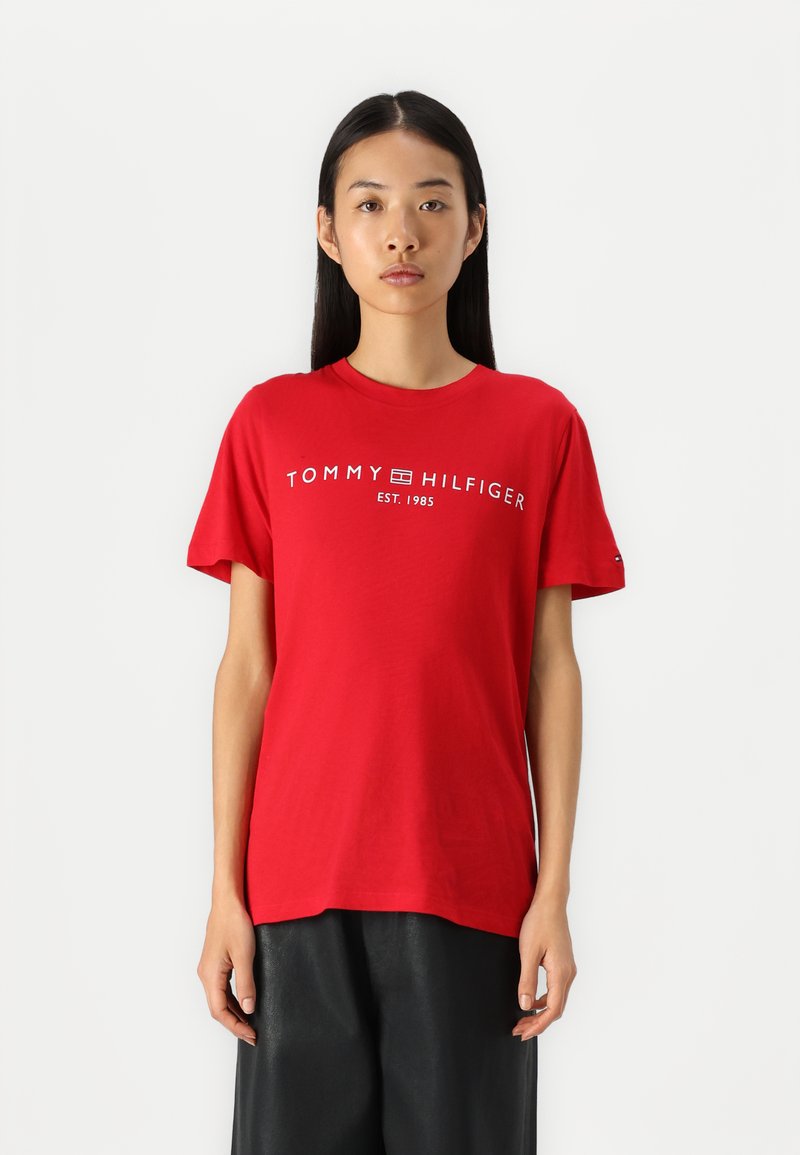 Red cotton T-shirt featuring a crew neck, short sleeves, and a white logo print "TOMMY HILFIGER EST. 1985" centered on the front.