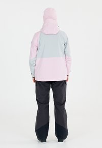 Leichte, wasserdichte Jacke in Pink und Grau, mit Kapuze und verstellbaren Bündchen. Ergänzt durch dunkle Cargo-Hosen mit einem enganliegenden Saum.