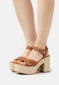 Sandali platform in suede marrone con ampie cinghie incrociate, fibbia per la caviglia, soletta in juta intrecciata e tacco testurizzato per maggiore stabilità.