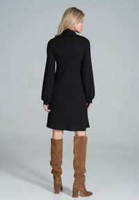 Zwarte geribbelde brei-jurk met een hoge kraag en lange puffmouwen, gecombineerd met tan suede kniehoge laarzen met een chunky hak.