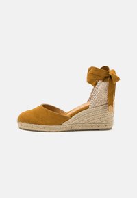 Hořčicově žluté plátěné espadrilky na klínku s pletenou jutovou podrážkou a texturovaným popruhem kolem kotníku, zavázané odpovídající stužkou.