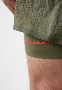 Green athletic shorts with a textured surface and perforations, featuring an inner tight in matching green with red branding accents.