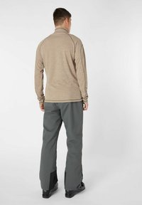 Beige Langarmoberteil mit hohem Kragen, kombiniert mit grauen Hosen mit schwarzen Akzenten an den unteren Beinen. Glatte Textur, lässiger Schnitt.