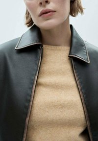 Black leather jacket with contrasting brown stitching and a pointed collar, paired with a beige knitted sweater. Zipper detail visible.