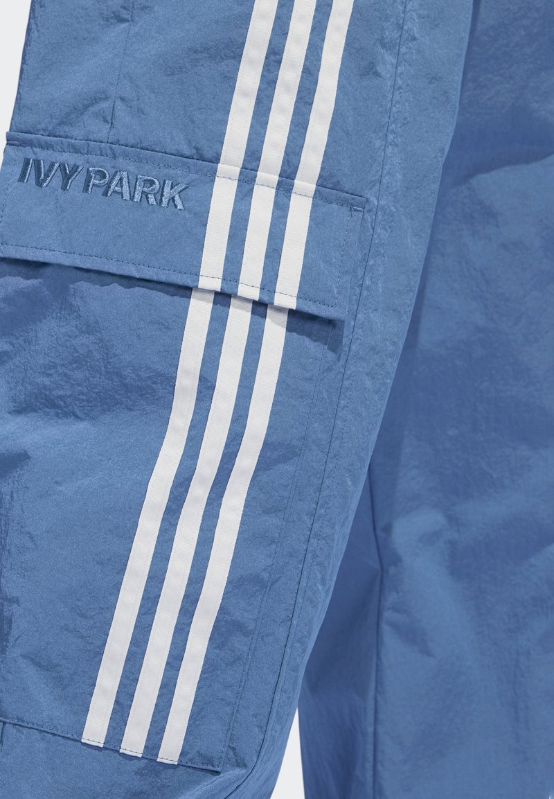 Lichtblauwe cargobroek met drie witte strepen aan de zijkant, gestructureerde stof en een "IVY PARK" logo geborduurd in het materiaal.