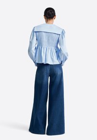 Világoskék blúz széles gallérral és gyűrt, gumis hátrésszel, sötétkék, bő szárú farmerrel párosítva. Sima anyag, bő szabás, finom textúra.